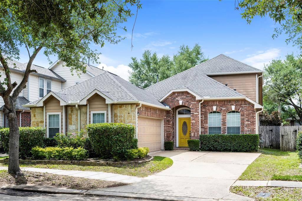 This charming two-story home features a mix of brick and stone exterior with a welcoming yellow front door. It includes a two-car garage, well-maintained landscaping, and mature trees, offering great curb appeal in a quiet neighborhood.