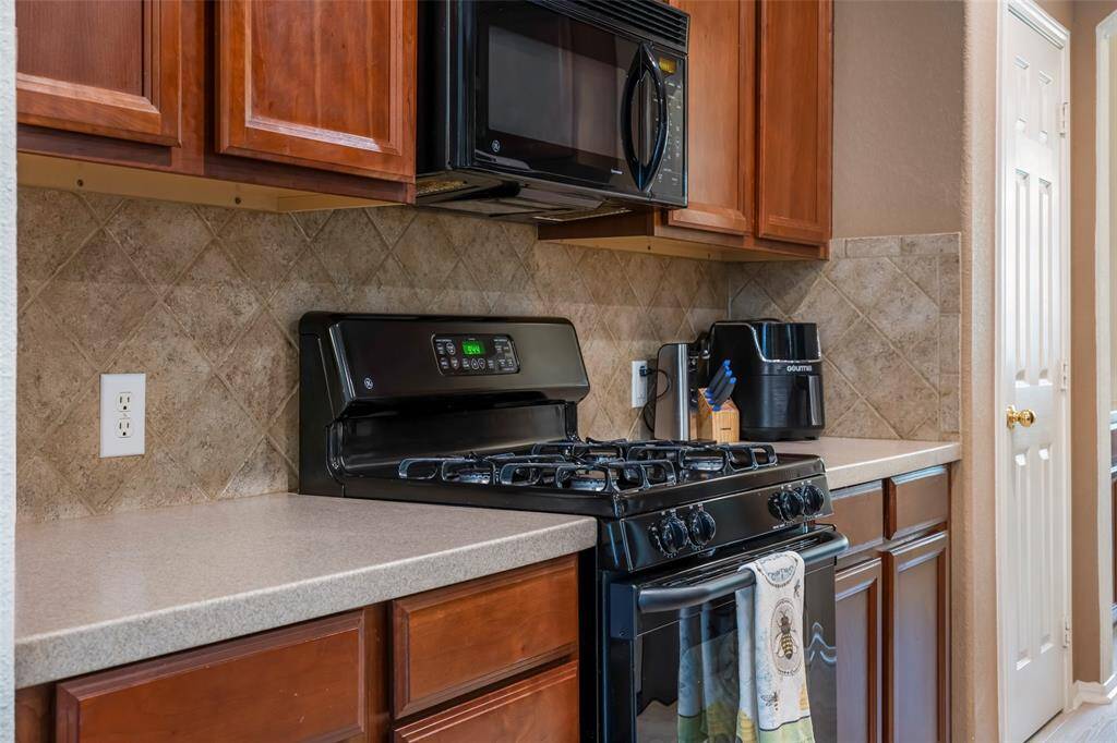 This kitchen features warm wooden cabinetry, a sleek black gas stove with matching microwave, and a neutral tiled backsplash for a classic and functional cooking space.