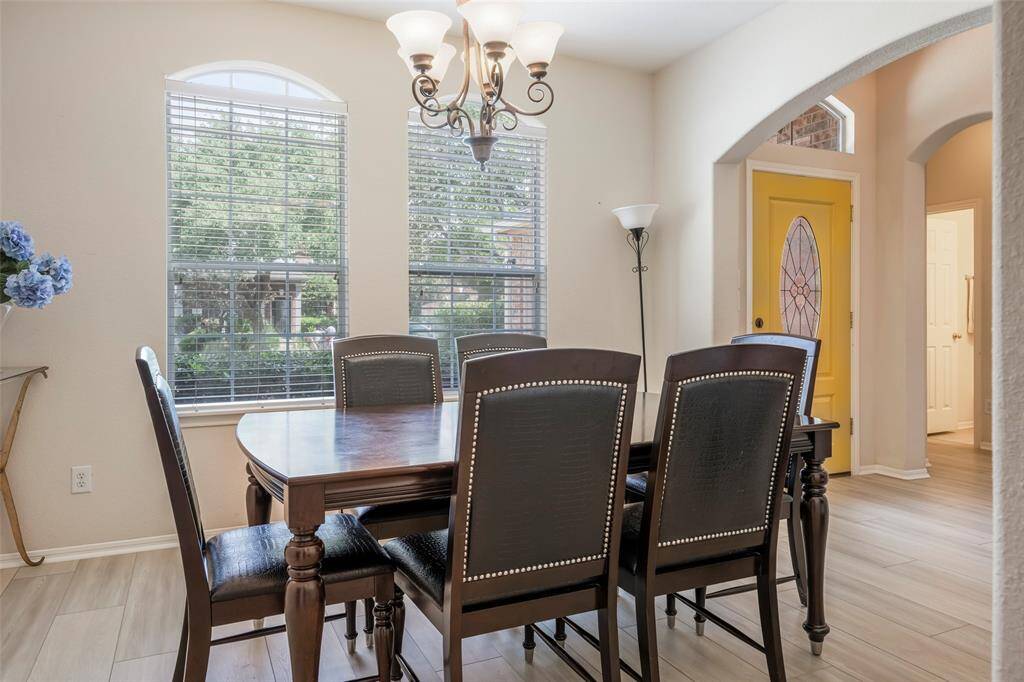 This photo showcases a bright dining area with large windows, a chandelier. The room features light wood flooring and is adjacent to an entryway with a distinctive yellow door, creating a welcoming and stylish ambiance.
