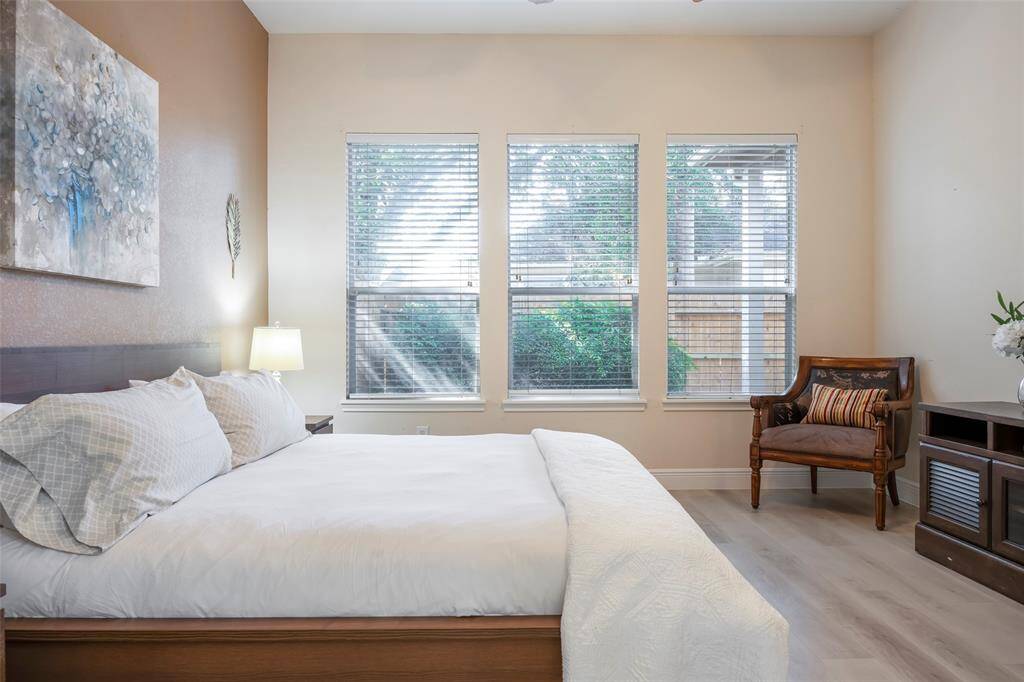 This bedroom features a cozy atmosphere with soft lighting, and tasteful decor. Three large windows allow natural light to brighten the space, complemented by light walls and flooring.