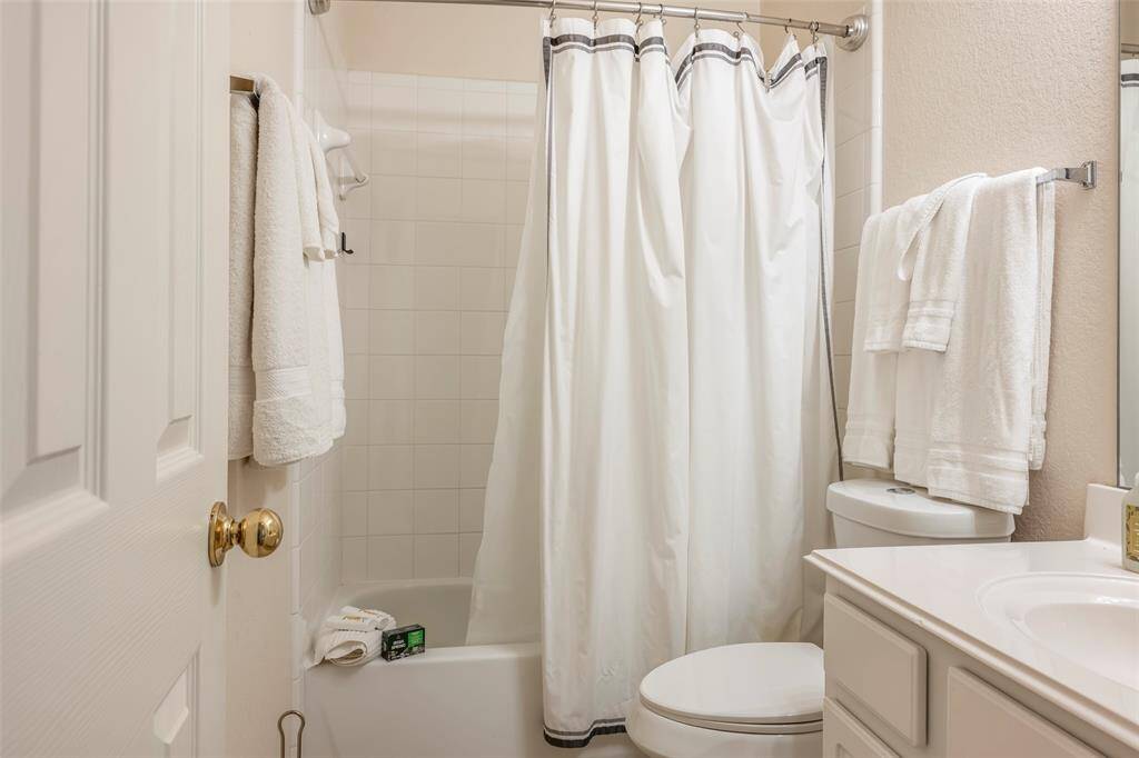 This bathroom features a clean, neutral design with a white tile shower, white curtain, and matching towels. It includes a bathtub, toilet, and a vanity with storage space, creating a bright and functional space.
