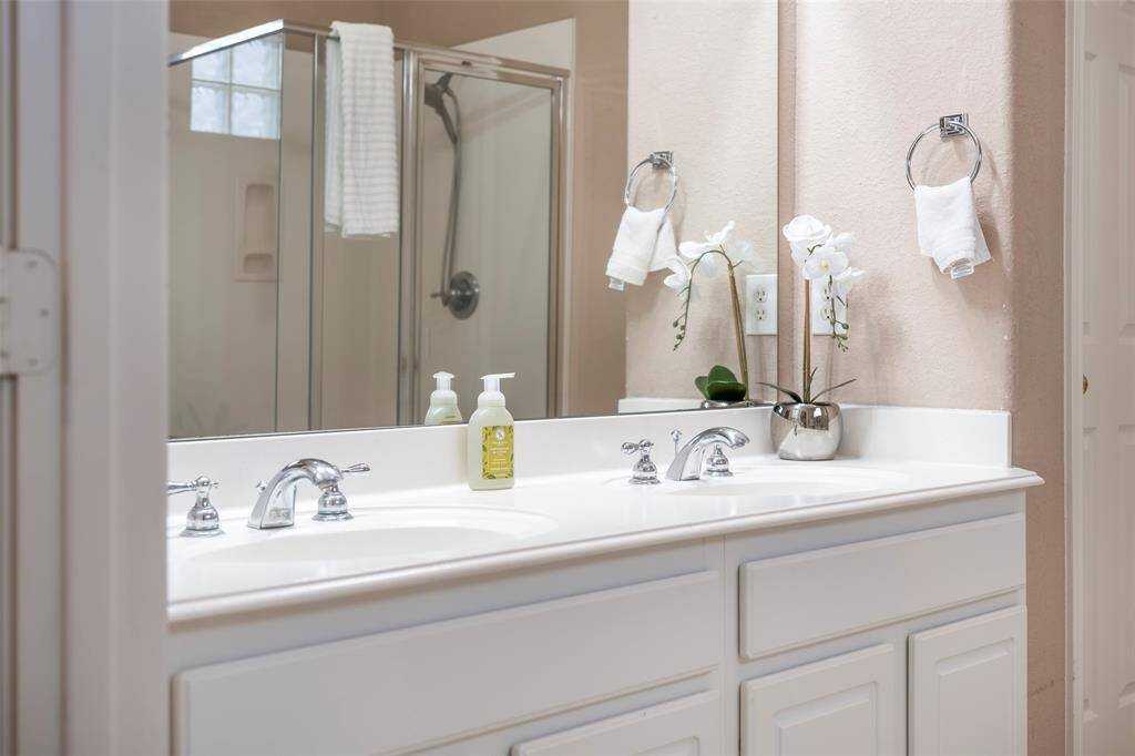 This bathroom features a dual-sink vanity with sleek chrome fixtures, a large mirror, and a glass-enclosed shower. The neutral color palette and natural light create a bright, inviting space.