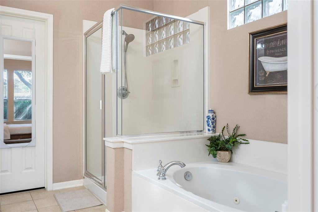 This bathroom features a glass-enclosed shower and a separate bathtub, accented with decorative art and a plant. The neutral color scheme and natural light create a serene atmosphere.
