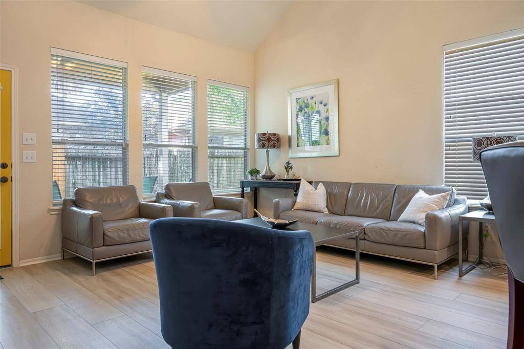 This living room features abundant natural light from large windows. It has neutral tones and a welcoming atmosphere, perfect for relaxation.