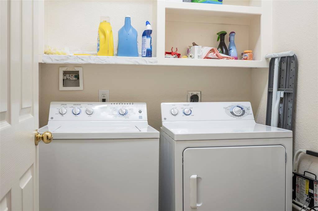 This photo shows a compact laundry area featuring a washing machine and dryer, with shelves above for storage of cleaning supplies.