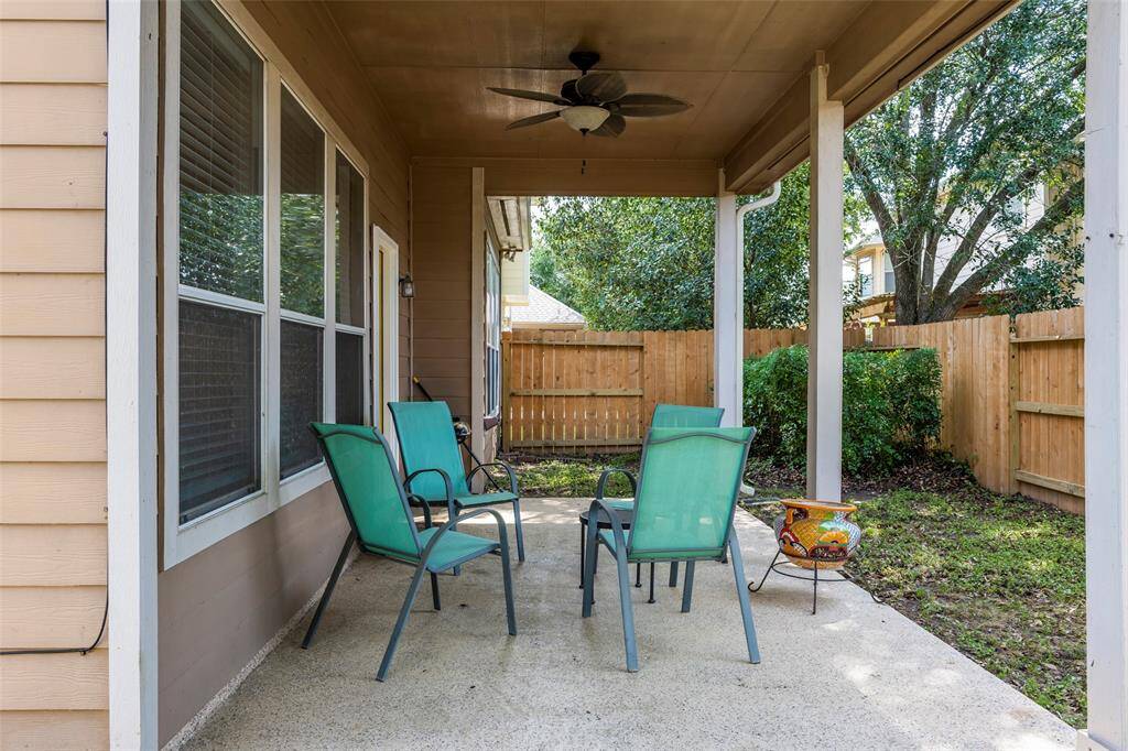 This photo shows a cozy covered patio with seating, a ceiling fan, and a view of a fenced backyard, offering a private outdoor space perfect for relaxation.