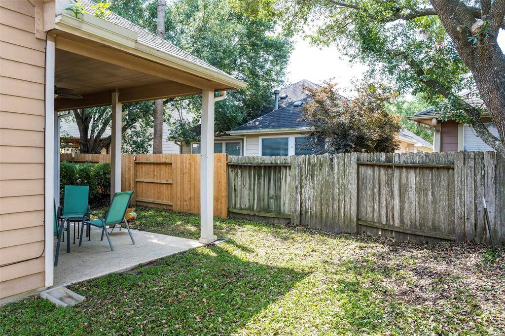 This backyard features a covered patio area, surrounded by a mix of wooden fencing. The space is shaded by mature trees, providing a cozy outdoor retreat.
