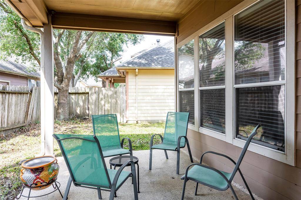 This is a cozy covered patio, offering a view of a fenced backyard with mature trees, perfect for relaxing outdoors.