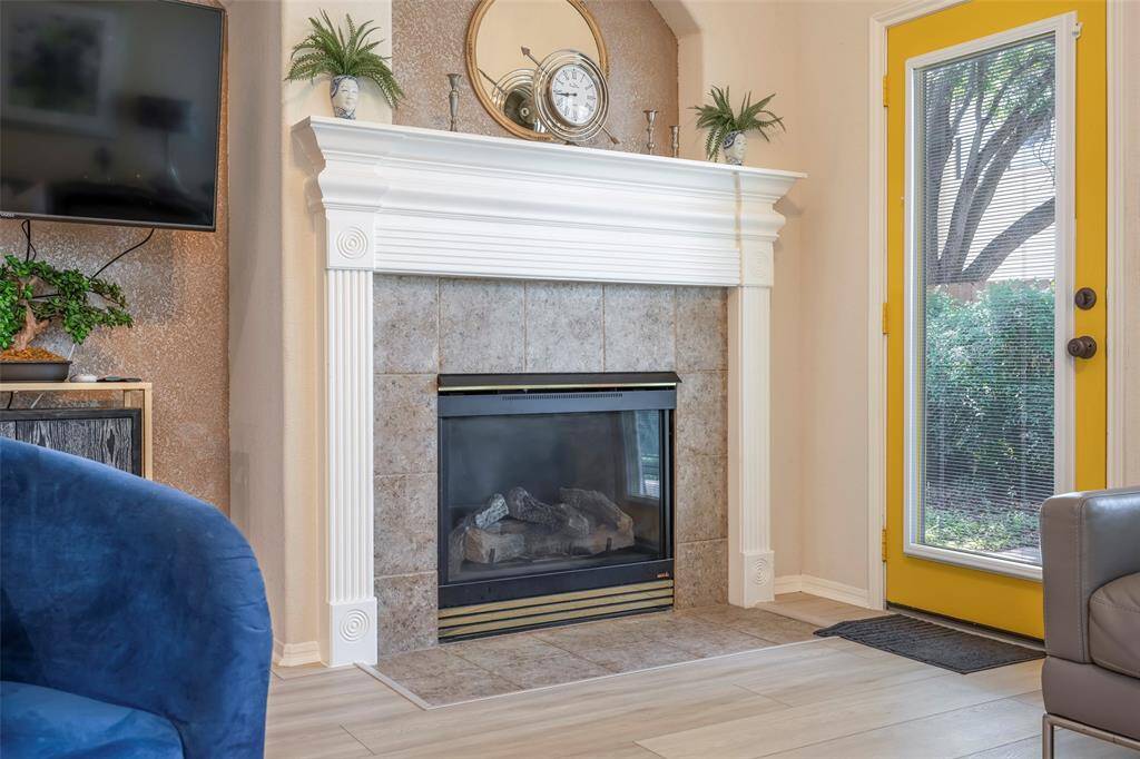 This cozy living space features a tiled fireplace with a classic white mantel, complemented by a stylish yellow-framed glass door that opens to a garden view. The neutral tones and modern decor create a welcoming atmosphere.