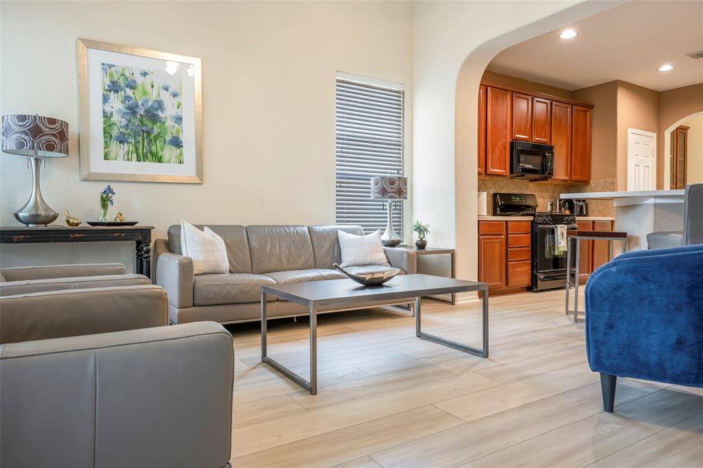 The photo showcases a modern, open-concept living area with light wood flooring.  The adjacent kitchen has warm wooden cabinetry, stainless steel appliances, and a breakfast bar, creating a seamless flow between spaces.