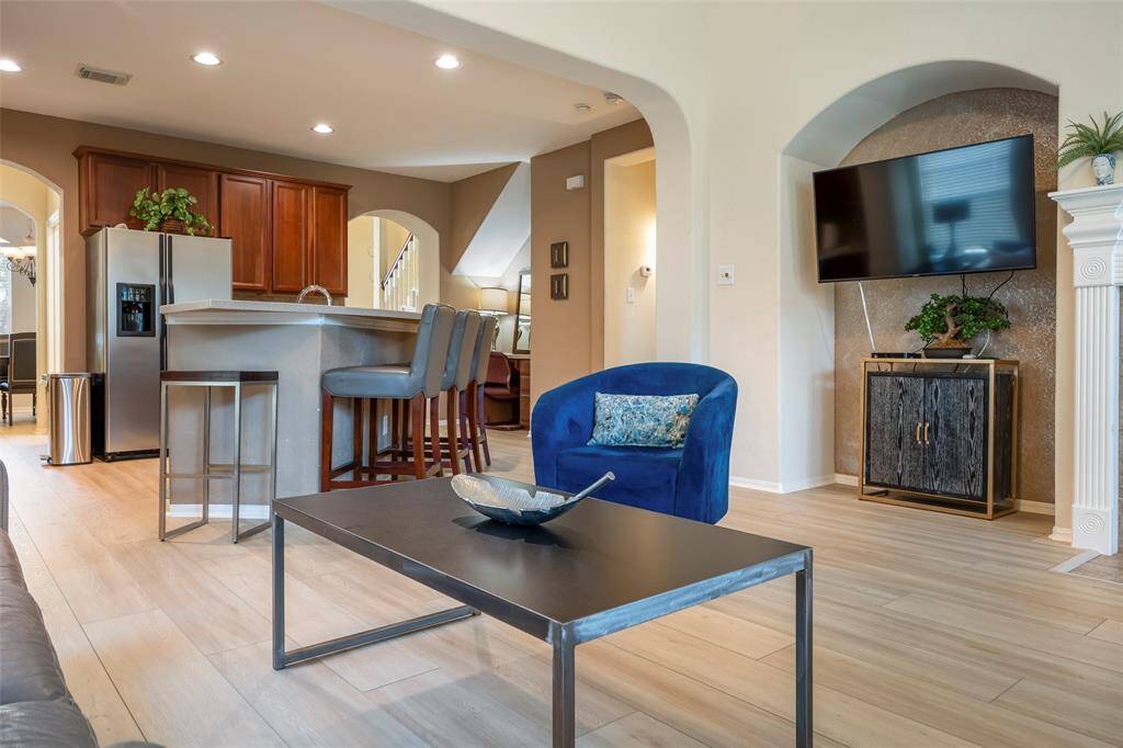 This photo showcases a modern open-concept living area with light wood flooring, a sleek kitchen with stainless steel appliances, and a breakfast bar.