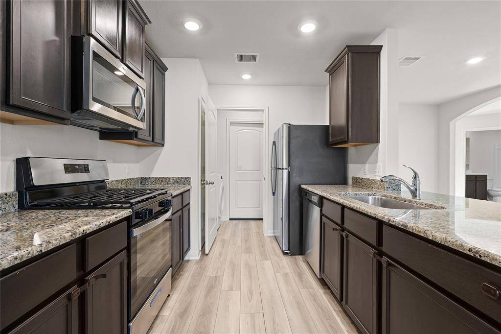 This modern kitchen features dark wood cabinetry, stainless steel appliances, and granite countertops. It has a sleek design with ample storage, a double sink, and recessed lighting, creating a bright and functional space.