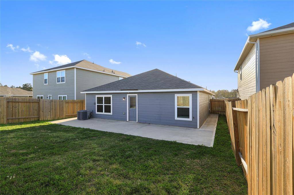 Backyard features a concrete patio and grassy area, ideal for outdoor activities or relaxation. The surrounding wooden fence provides privacy, and neighboring homes are visible on either side.