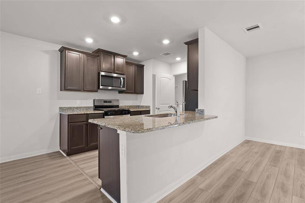 Modern kitchen with dark wood cabinets, granite countertops, and stainless-steel appliances. The open layout includes a breakfast bar and light wood flooring, creating a bright and inviting space.
