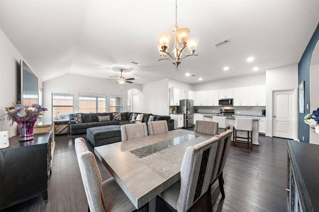 This photo showcases a spacious open-concept living area with a modern kitchen, dining, and living room. It features high ceilings, dark wood flooring, and abundant natural light from large windows. The kitchen has sleek white cabinets, stainless steel appliances, and a central island with bar seating.