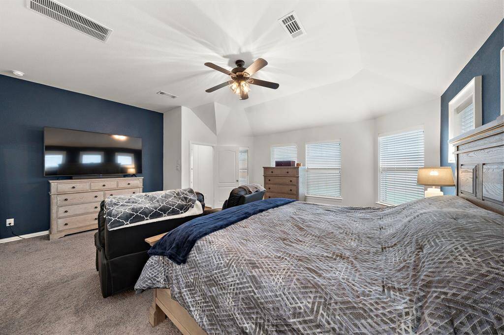 This spacious bedroom features a vaulted ceiling with a fan, a large window for natural light, and contemporary decor with a statement wall.