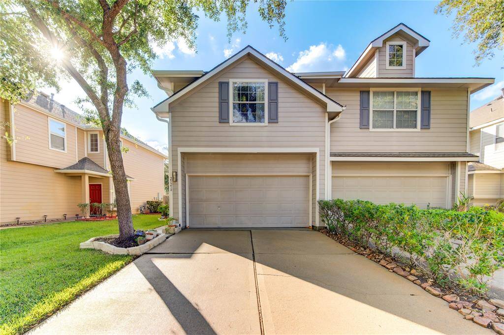 Charming two-story home with a double garage, set in a well-maintained neighborhood. Features a neatly paved driveway, manicured front lawn, and mature trees providing shade. The exterior is accented with neutral siding and shutters, offering great curb appeal.