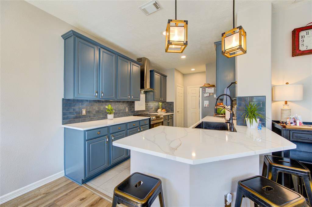 This kitchen features modern blue cabinetry, a sleek white countertop, and a stylish backsplash. It includes an island with bar seating and pendant lighting, creating an inviting space for cooking and entertaining.