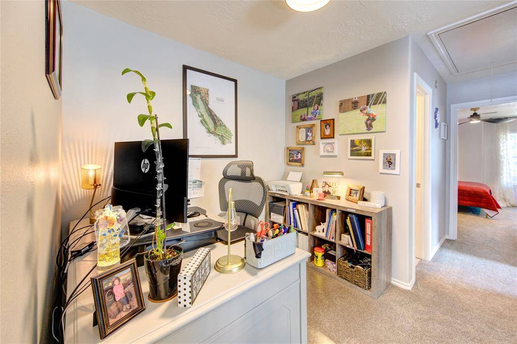 This photo showcases a compact yet functional home office with dual monitors, a comfortable chair, and ample desk space. The room features personal touches with wall art and family photos, creating a cozy and personalized workspace.