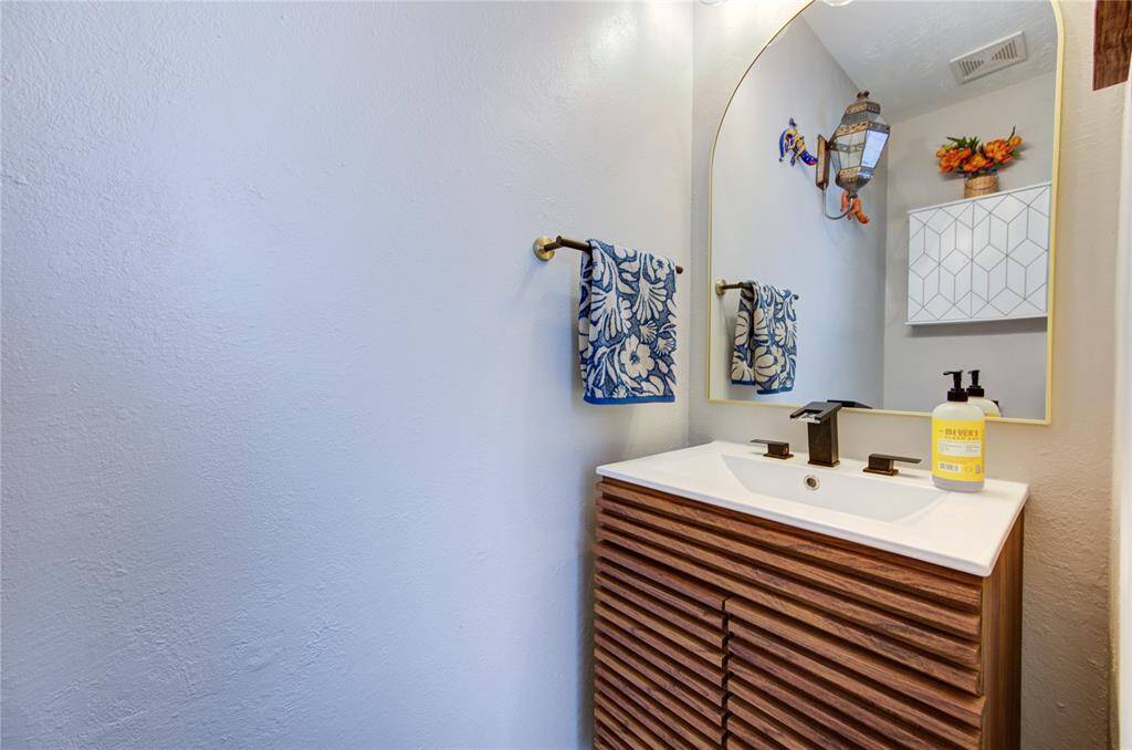 This bathroom features a modern vanity with a sleek, striped wooden design and contemporary black fixtures. It includes a large, arched mirror and is accented by floral hand towels and decorative wall elements, creating a fresh and inviting atmosphere.