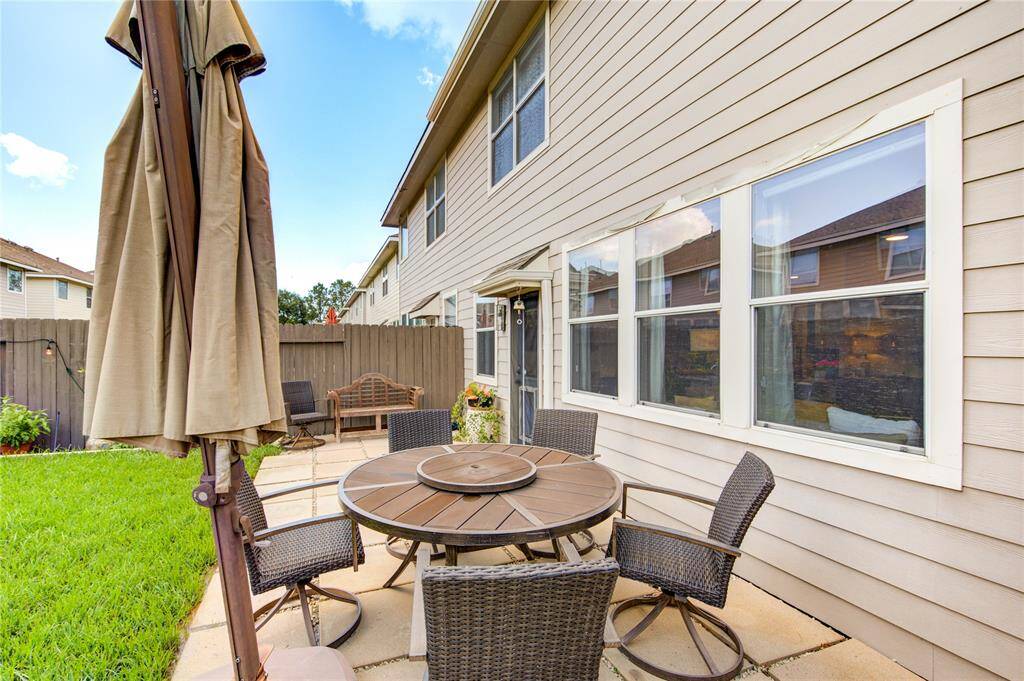 This photo showcases a cozy backyard patio featuring a round table with chairs, perfect for outdoor dining. The space is bordered by a wooden fence and a well-maintained grassy area, providing a private and inviting setting.