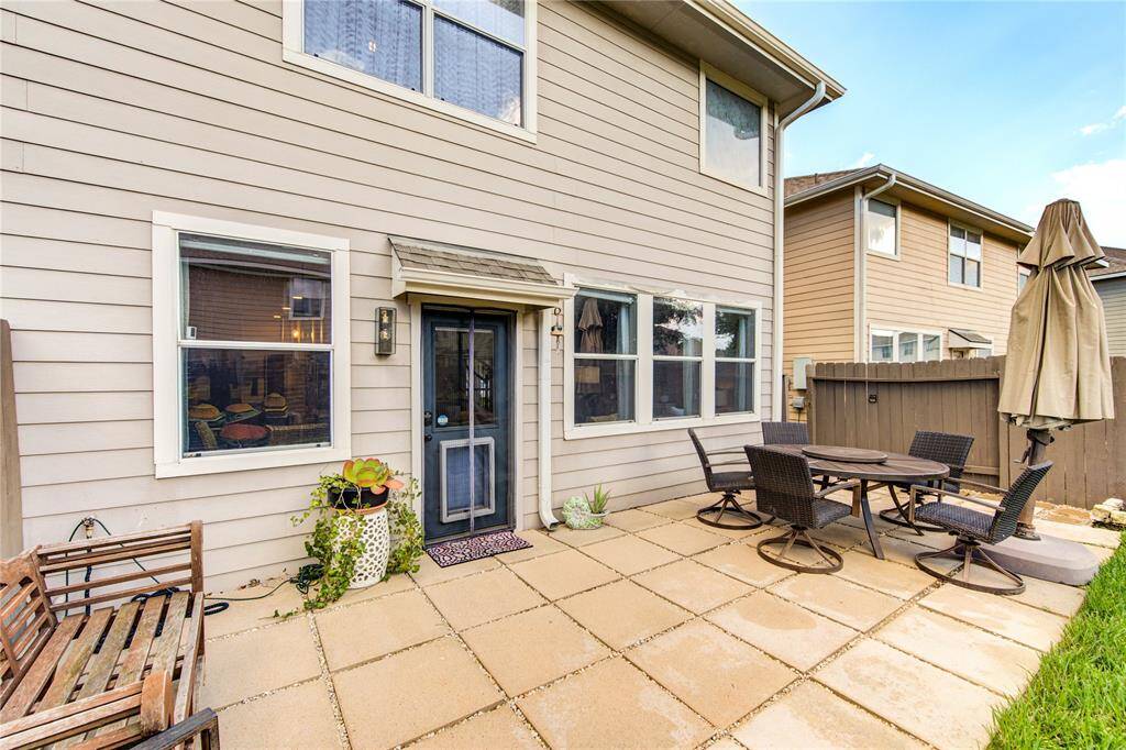 This photo showcases a cozy backyard patio with a table and chairs set, perfect for outdoor dining. It features a neatly paved area, a wooden bench, and is adjacent to a neatly maintained house exterior with large windows, offering a welcoming and functional outdoor space.
