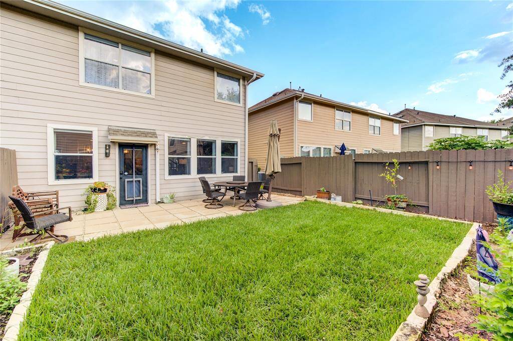 This backyard features a well-maintained lawn, a cozy patio with seating and an umbrella, and a privacy fence, perfect for outdoor relaxation and entertaining.
