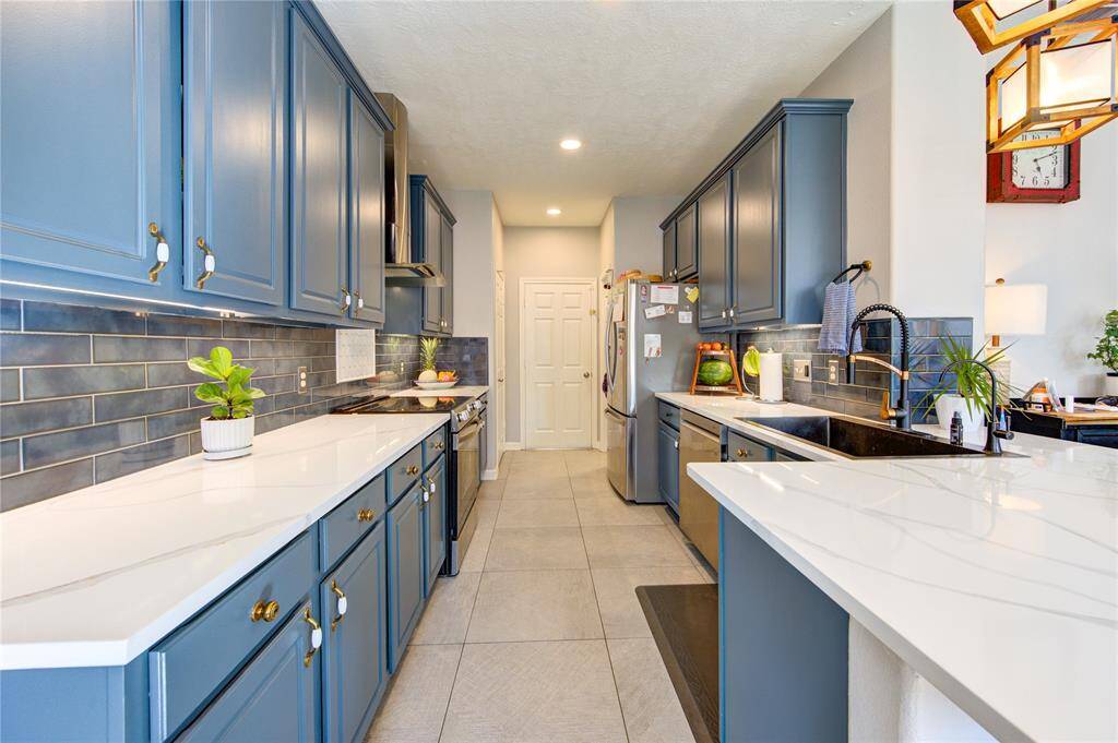 This kitchen features modern blue cabinetry, sleek white countertops, and a stylish subway tile backsplash. It's equipped with stainless steel appliances and has ample lighting, creating a bright and inviting space.