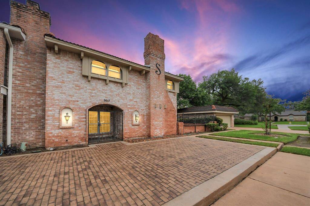 Front elevation at sunsetBeautifully lit brick exterior with a timeless design and gated entry. This charming end-unit townhome offers a warm welcome with a dramatic chimney detail and sunset ambiance.