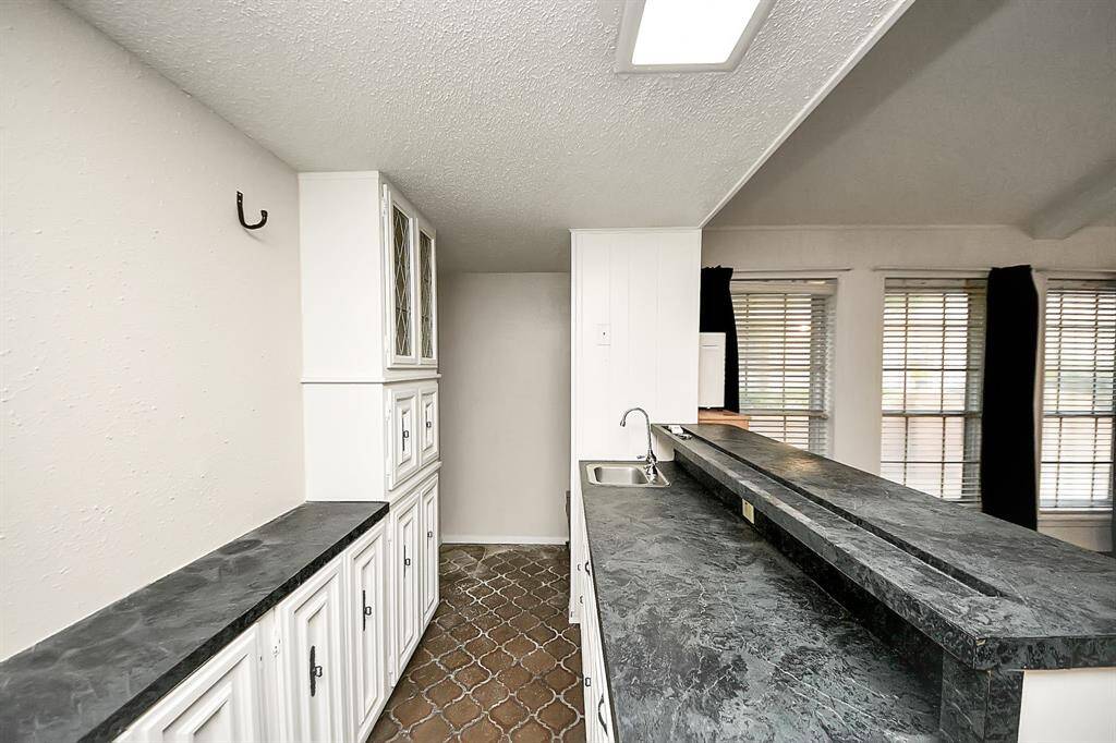 Charming wet bar area with abundant counter space, upper and lower cabinetry, a sink, and vintage glass-front accents—perfect for entertaining or crafting your favorite drinks.