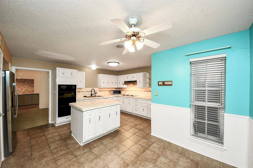 Kitchen with Dining Nook – Enjoy this bright and open kitchen featuring white cabinetry, a large center island, tile countertops, and an adjacent breakfast area with large windows.