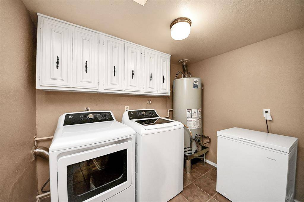 Spacious laundry room equipped with a washer, dryer, water heater, and deep freezer. Upper cabinetry offers generous storage to keep cleaning essentials organized and out of sight.