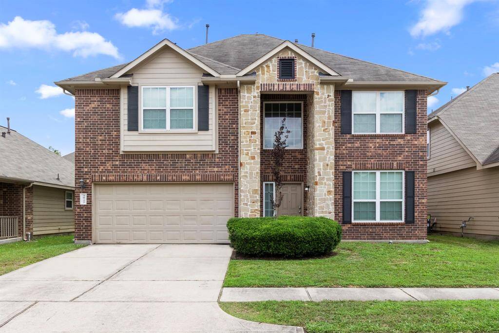 This two-story home features a brick and stone exterior, a two-car garage, and a neatly landscaped front yard. It offers a welcoming and well-maintained appearance, ideal for family living.