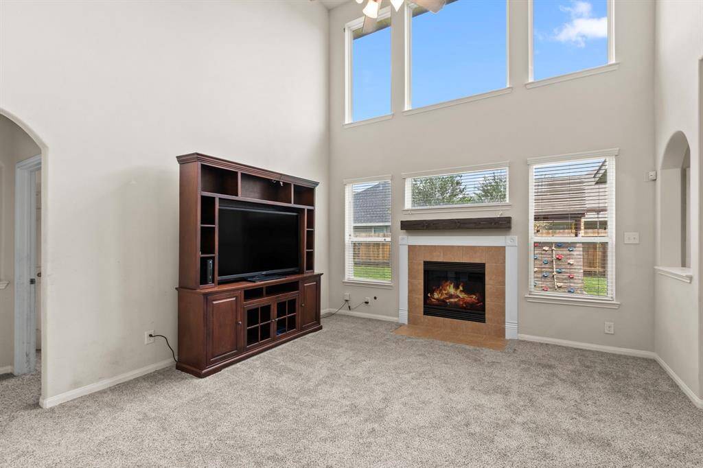 Bright living room with high ceilings, large windows, and a cozy fireplace. Features a built-in entertainment center and carpeted flooring.