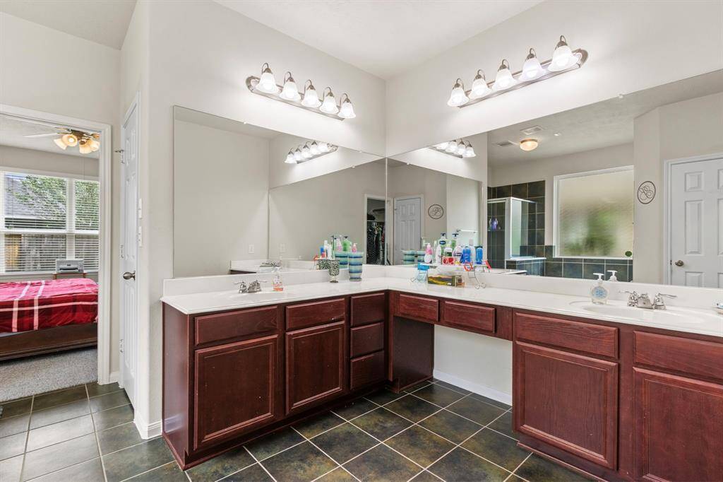 This spacious bathroom features dual sinks with dark wood cabinetry, large mirrors, and modern lighting. It connects to a bedroom with natural light and has a tiled floor for easy maintenance.