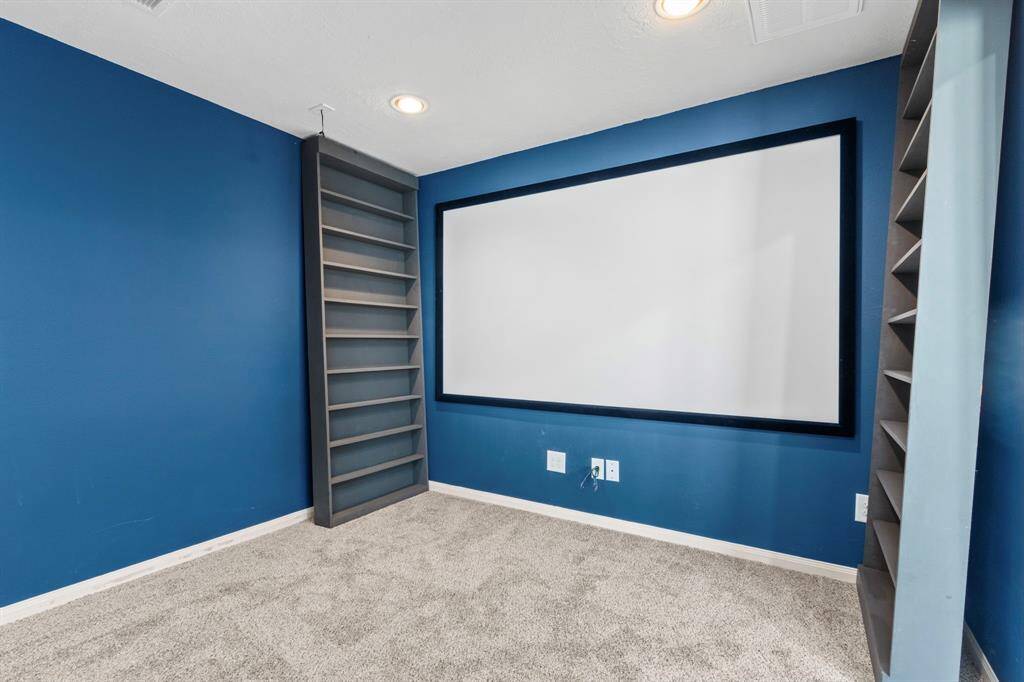 This room features a cozy home theater setup with blue walls, recessed lighting, and built-in shelving. Ideal for entertainment, it includes a large screen and plush carpeting for comfort.