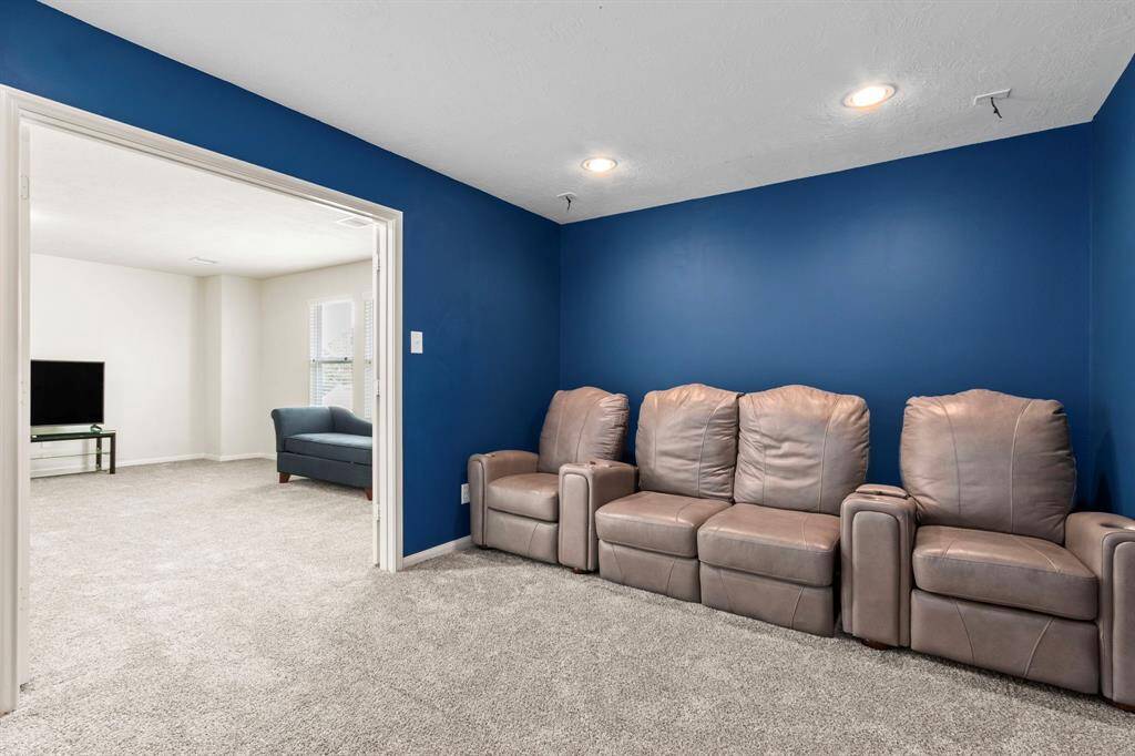 This cozy home theater features a bold blue accent wall and comfortable leather recliners, perfect for movie nights. Adjacent is a bright living space with neutral walls and carpet, offering a TV setup and additional seating.