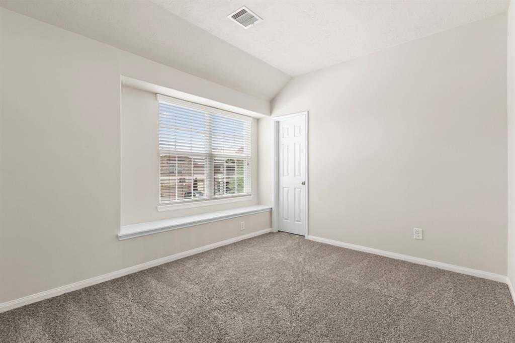 Bright room with neutral walls and carpet, featuring a large window with blinds. There's a small closet door and a ledge beneath the window, creating a cozy nook.
