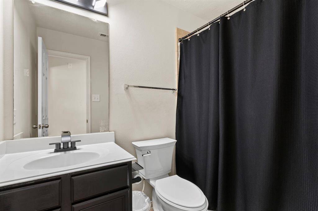 This bathroom features a sleek design with a modern vanity, a large mirror, and a clean white sink. It includes a toilet and a shower area with a black curtain, offering a stylish contrast against the neutral walls.