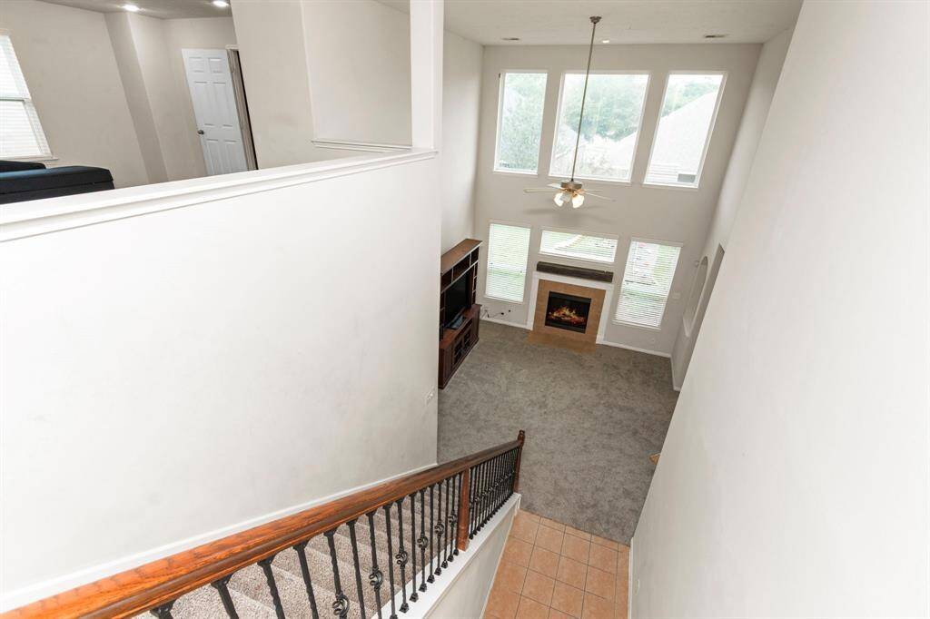 This photo showcases a spacious, two-story living area with large windows, providing ample natural light. The room features a cozy fireplace and an open view from the upper level, complemented by a wooden staircase with iron railings.