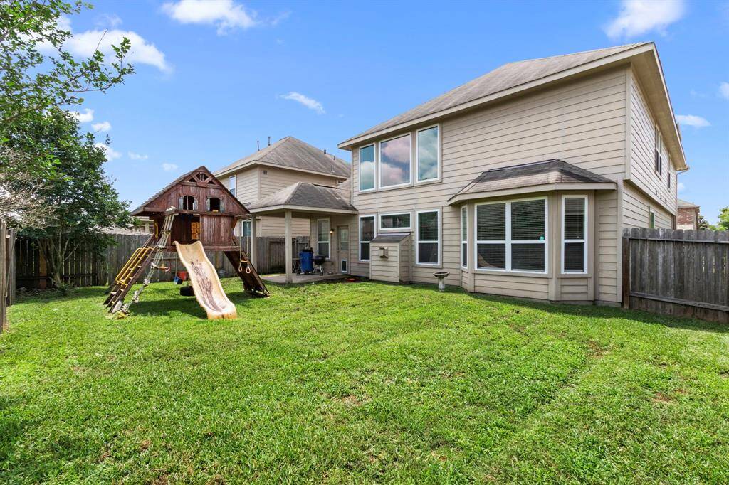 This photo showcases a spacious backyard with a well-maintained lawn, featuring a children's playset with a slide. The back of the house has large windows and a fenced perimeter for privacy, offering a family-friendly outdoor space.