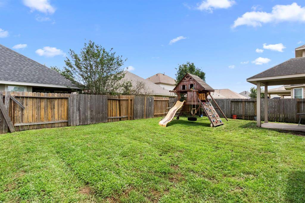 Spacious backyard with a well-maintained lawn, featuring a wooden playset for kids. The area is enclosed with a wooden fence, offering privacy and a safe play environment. Ideal for family activities and outdoor enjoyment.