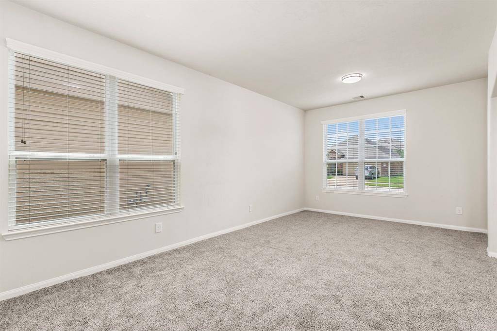 Bright and airy room with neutral walls and carpet, featuring large windows with blinds that offer ample natural light.