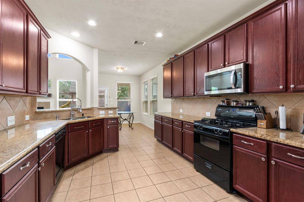 Spacious kitchen with rich wood cabinetry, granite countertops, and modern appliances. Features a gas range, ample storage, and a bright, open layout with tiled flooring. Ideal for cooking and entertaining.