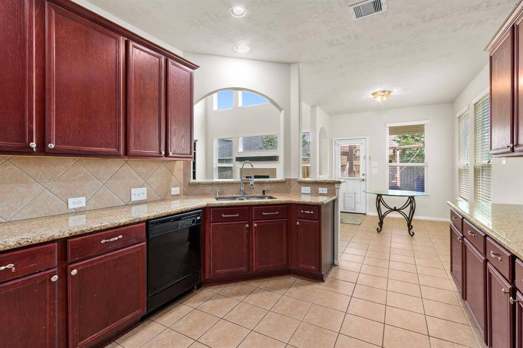 This bright kitchen features rich wood cabinetry, granite countertops, and a central island with a sink. It opens to a dining area with large windows and tile flooring, creating a spacious and inviting atmosphere.