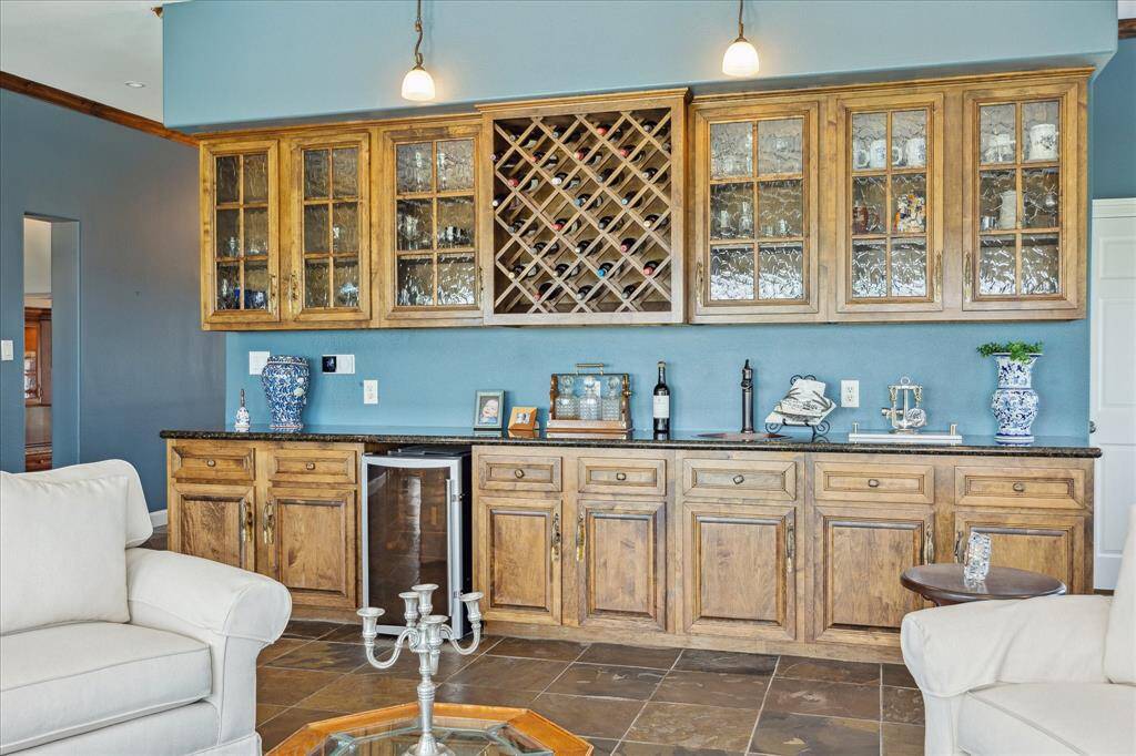 The built-in bar/entertainment cabinetry in the family room includes glass front upper cabinets and wine rack and lower drawer and cabinet storage with granite counter top, copper bar sink and wine fridge.