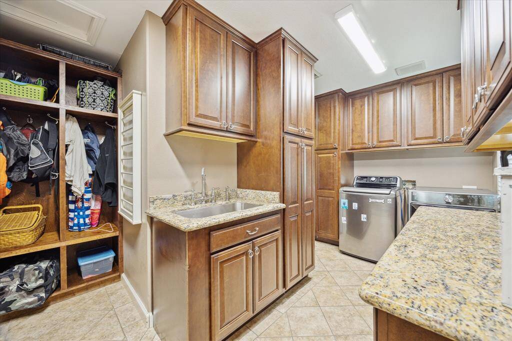 The indoor laundry room has an extensive amount of upper level storage cabinetry, broom/vacuum cabinet, granite topped folding shelf, a large undermount stainless steel sink, open storage locker and can be accessed from two entry points.