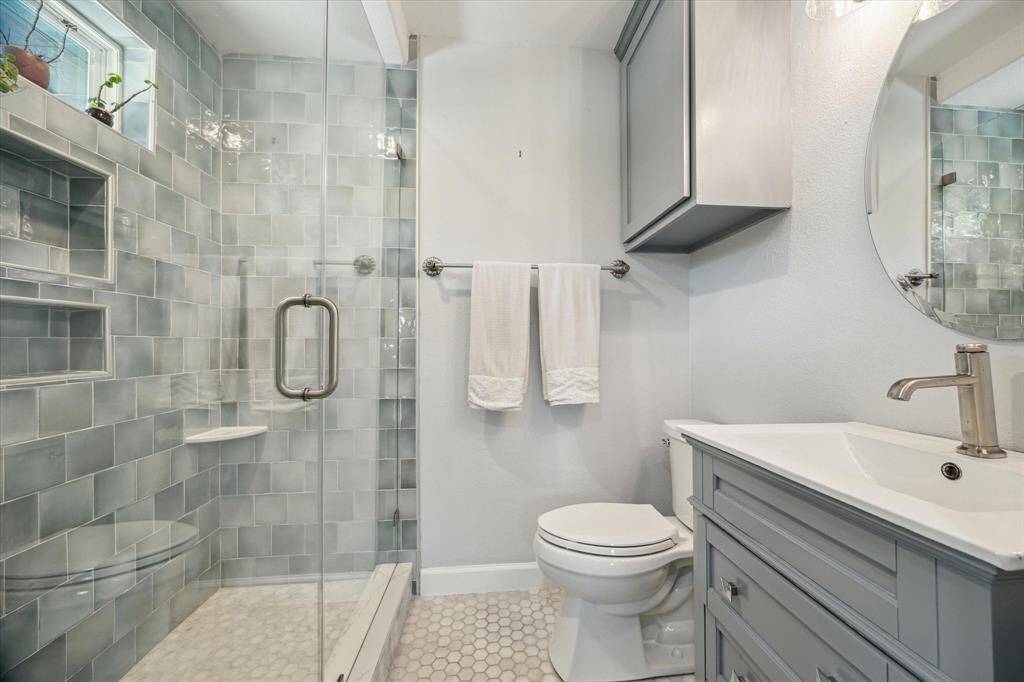Full bath 4 is located in bedroom 4. Features include an updated shower with double soap niche, built-in corner shelf, transom window and frameless glass enclosure, an updated vanity cabinet with integrated sink and tile floor.