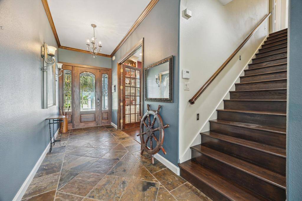 This view from within the entry hall shows the Mahogany entry door with arched glass window, matching Mahogany and glass side-lite windows and slate tile floor. The French doors at the right of this photo lead to the home office/study. Stairs at the right of this photo lead to the upper level primary suite.