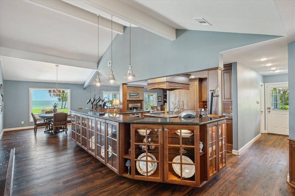 This is the view when entering the kitchen from the entry hall. The outer perimeter of the kitchen features wrap-around, lighted glass front cabinets with slab granite tops that match all kitchen counter surfaces. Triple nautical style pendant light fixtures accent these cabinets.